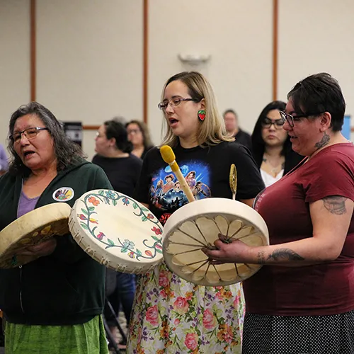 women chanting and beating drums
